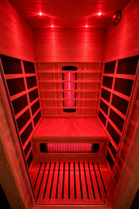 Interior of a 1 person infrared sauna with natural wood walls, black heater panels and red light therapy illumination