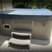 Charcoal grey spa pool cover fitted on an outdoor spa, shown with securing straps and entry steps in a real backyard setting.