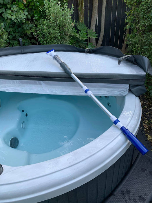 Rechargeable cordless spa vacuum resting across the edge of a white spa pool with insulated cover in the background